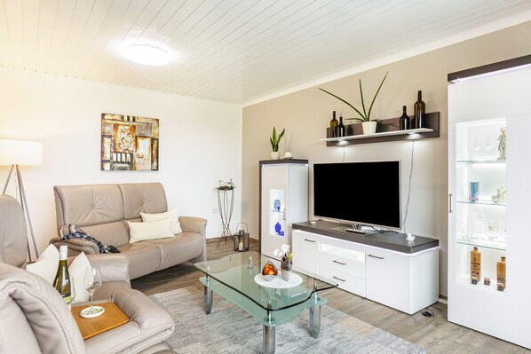 Una sala de estar moderna con un sofá, una mesa de centro de vidrio, un televisor de pantalla plana y un mueble con puertas de cristal.