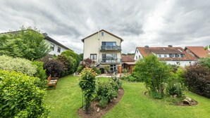 A two-story house with a balcony, surrounded by a well-maintained garden with various plants and a lawn. - Apartment 'Landblick' with Shared Garden, Balcony and Wi-Fi (Homberg (Efze))