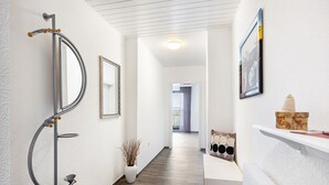 A hallway with a coat rack, a mirror, a potted plant, a shelf with decorative items, and a framed picture on the wall. - Apartment 'Landblick' with Shared Garden, Balcony and Wi-Fi (Homberg (Efze))
