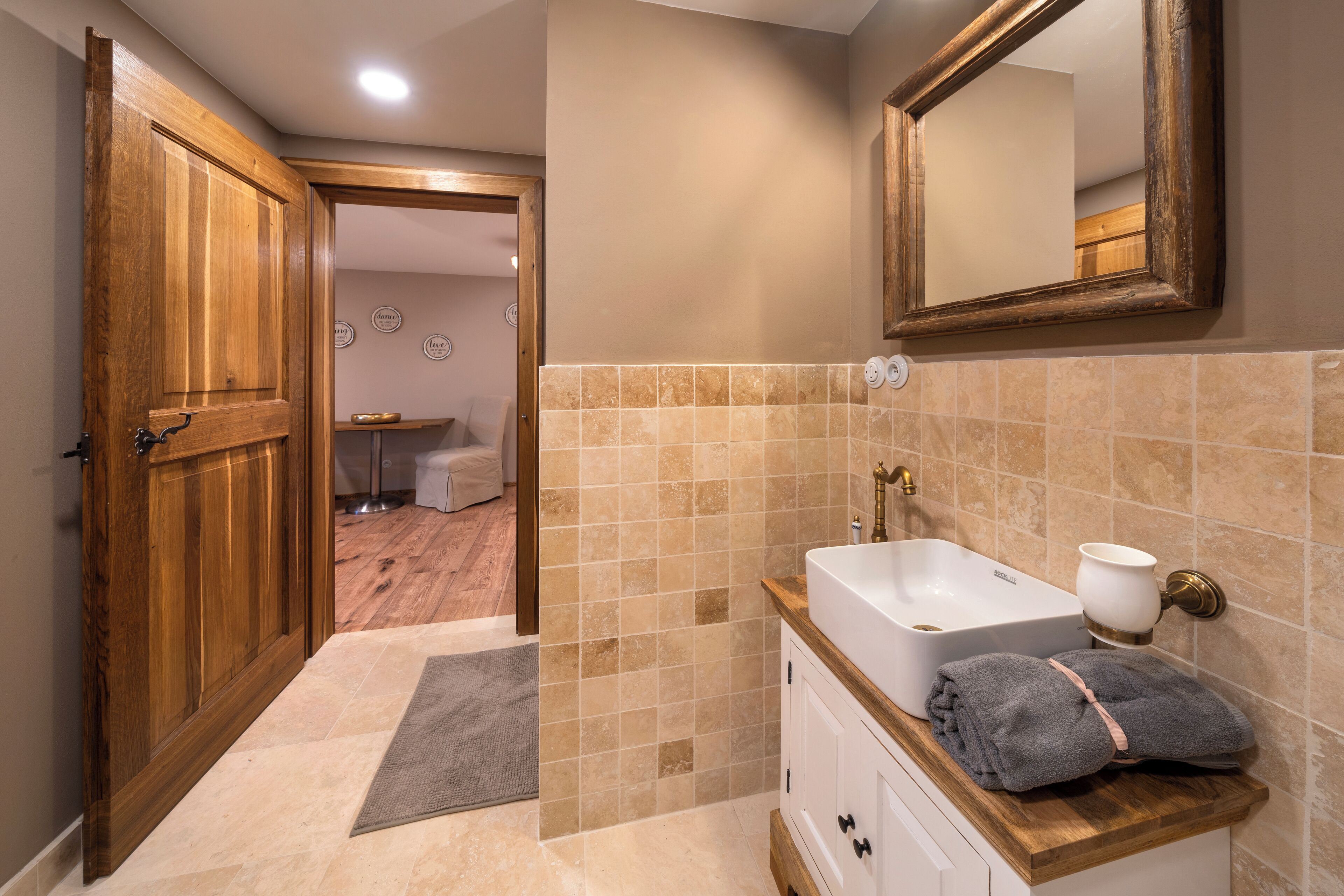 A bathroom with a wooden door, beige tiles, a white sink, and a towel on the counter.