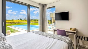 Une chambre d’hôtel avec un grand lit, un bureau, une télévision et une vue sur une piscine et la campagne environnante.