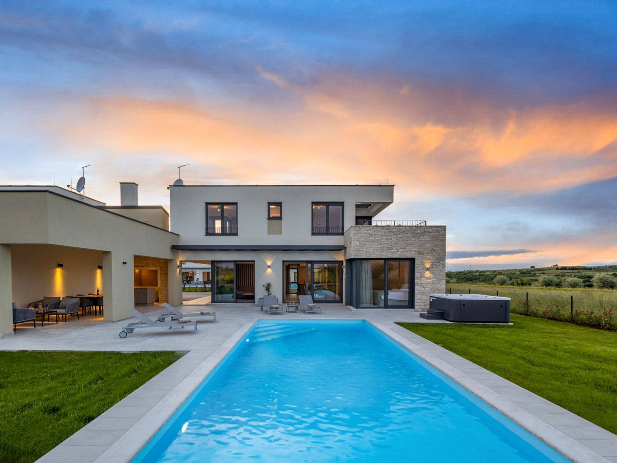 A modern two-story house with a swimming pool, outdoor seating, and a view of the countryside.