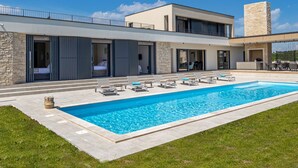 Un bâtiment moderne à deux étages, doté d’une piscine, d’un espace extérieur aménagé et d’une tour en pierre.