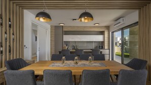 Une salle à manger moderne avec une table en bois, six chaises grises à revêtement rembourré et des luminaires suspendus.