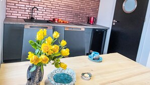 Een keuken met een tegelwand, een spoelbak, een koffiezetapparaat en een kleine tafel met een vaas gele rozen.