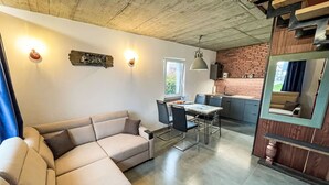 Een moderne woonkamer met een hoekbank, een eettafel met stoelen, een keuken met een tegel achterwand en een grote spiegel.