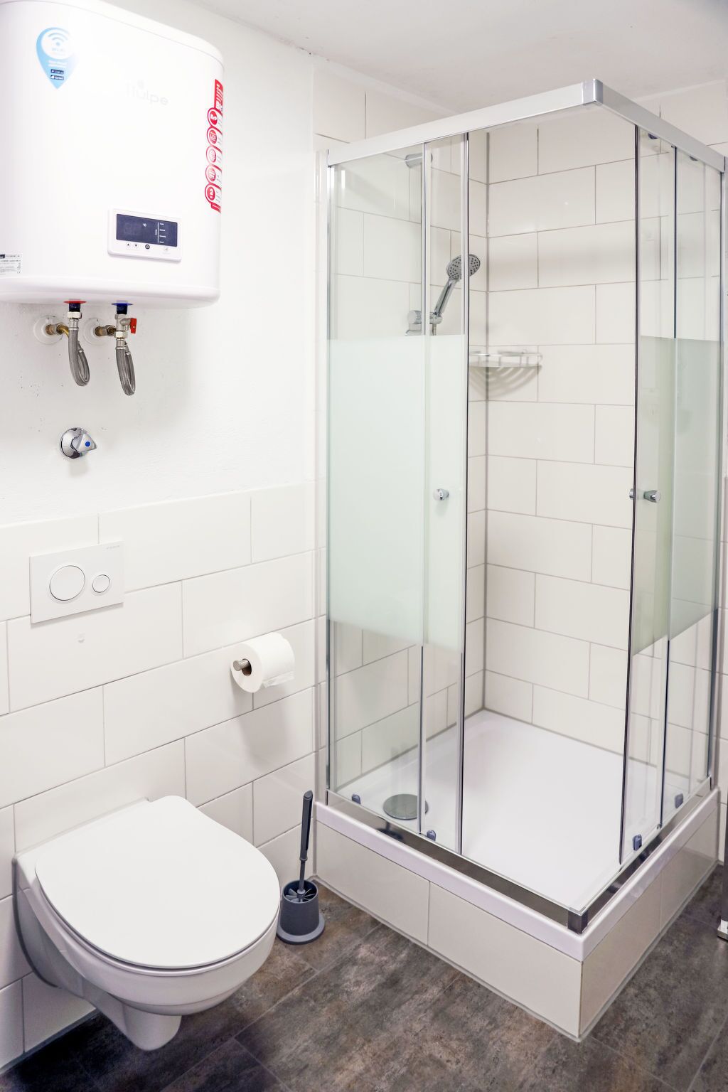 Un baño moderno con ducha acristalada, inodoro y calentador de agua.