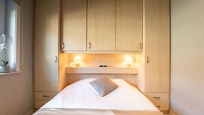 Une chambre à coucher avec un lit, des armoires en bois, une table de chevet avec une lampe et une fenêtre agrémentée d’une plante.