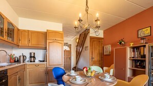 A kitchen with wooden cabinets, a dining table with chairs, and a chandelier. - Geluid van de zee by Interhome (De Haan)