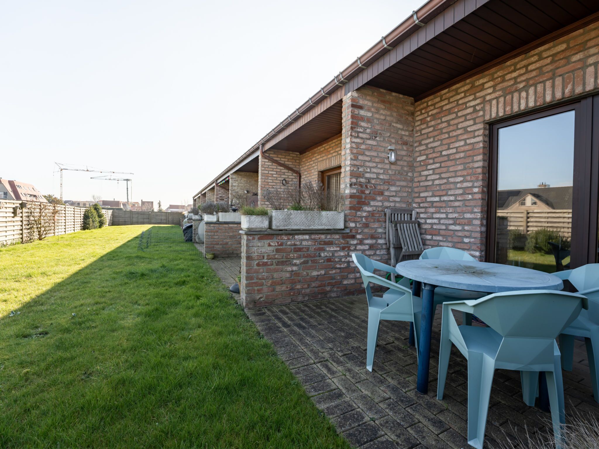 A patio area with a brick wall, a small table with chairs, and a grassy lawn.