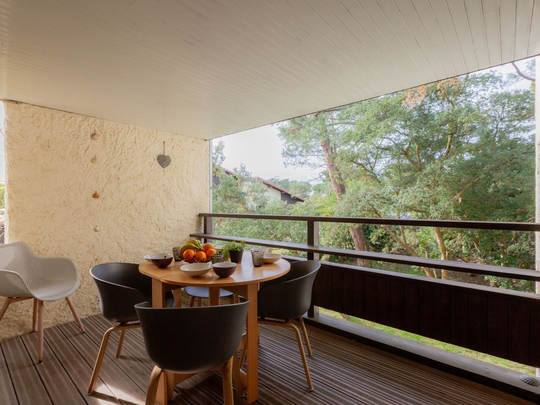 Ein Balkon mit Holztisch und -stühlen, einer Obstschale und Blick auf Bäume.