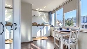 A modern kitchen with white cabinets, a wooden countertop, and a view of the city through large windows.