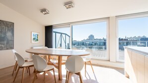 A modern dining area with a round table and six chairs, large windows with a city view, and a wooden floor.