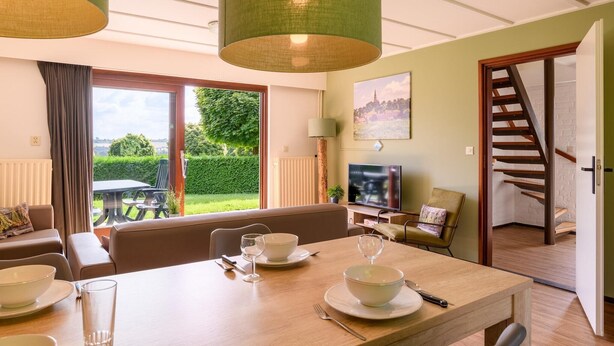 A dining area with a table set for two, a sofa, a TV, and a staircase leading to another room. - Bungalow in Reevallis near Scenic Hills (Vijlen)