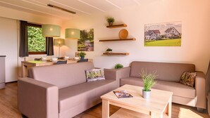 A modern living room with a sofa set, a dining table, and a coffee table. There are plants on shelves and a painting on the wall. - Bungalow in Reevallis near Scenic Hills (Vijlen)