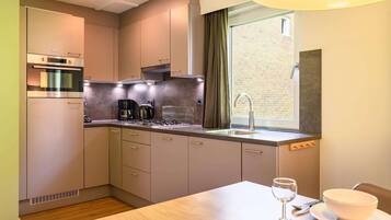 Una cocina compacta con electrodomésticos modernos, una ventana con cortinas y una zona de comedor con mesa y sillas.
