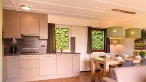 A modern kitchen with built-in appliances, a dining area with a table and chairs, and large windows with a view of greenery. - Bungalow in Reevallis near Scenic Hills (Vijlen)