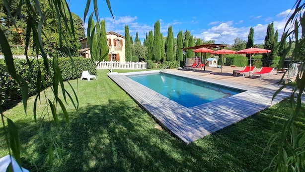 Un espace piscine doté d’une terrasse en bois, de chaises longues rouges et d’une clôture blanche.