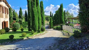 Une allée de gravier mène à une maison entourée d’une clôture en bois et agrémentée d’une pergola.