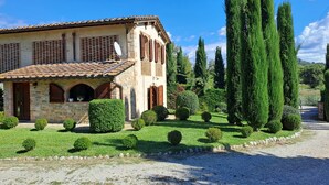 Une maison en pierre avec un toit de tuiles, des fenêtres en arc de cercle et une allée gravillonnée.