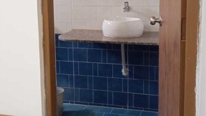 A bathroom with a white sink, blue tiles, a wooden door, and a mirror. - Elis Home Stayz (Ahmedabad)