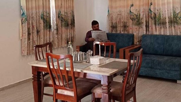 A dining area with a wooden table and chairs, a blue sofa, and two pendant lights. - Elis Home Stayz (Ahmedabad)
