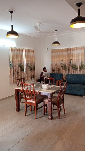 A dining area with a wooden table and chairs, a blue sofa, and two pendant lights. - Elis Home Stayz (Ahmedabad)