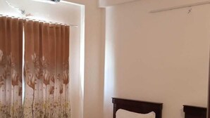 A hotel room with two beds, a ceiling fan, an air conditioning unit, and a window with curtains. - Elis Home Stayz (Ahmedabad)