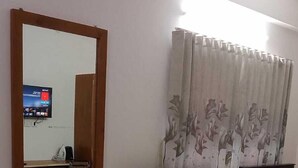 A hotel room with a bed, a wooden nightstand, a mirror, a television mounted on the wall, and a window with curtains. - Elis Home Stayz (Ahmedabad)