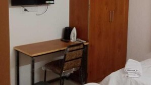 A bedroom with a wooden wardrobe, a desk with a chair, a television mounted on the wall, and two beds with white linens. - Elis Home Stayz (Ahmedabad)