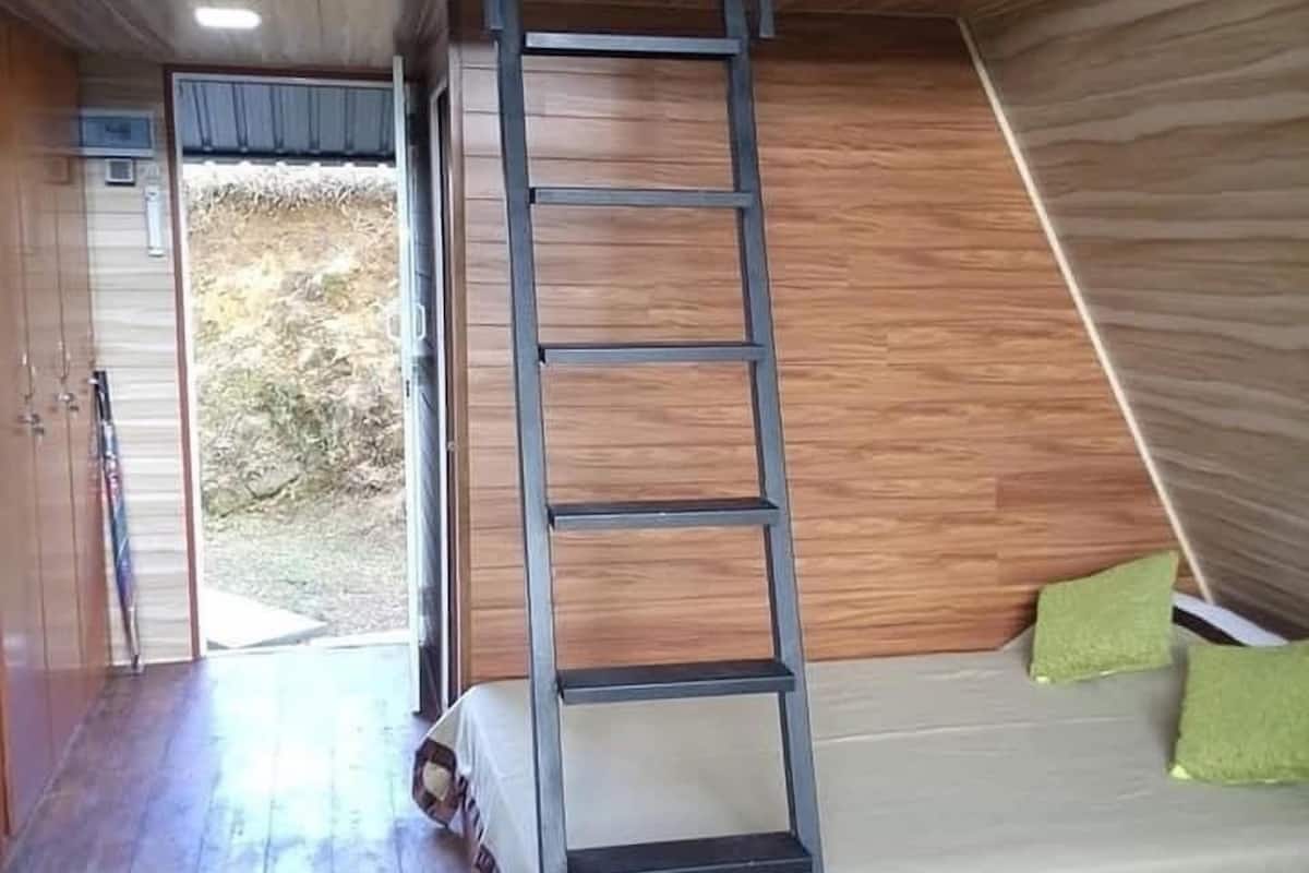 A room with a wooden floor, a sofa with green cushions, and a ladder against the wall.