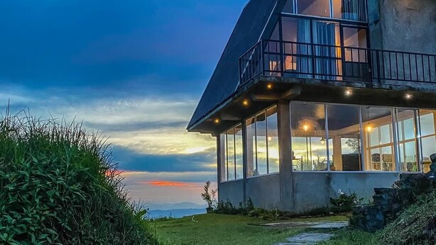 Een modern huis met een grote glazen gevel, een balkon en een stenen pad dat naar de ingang leidt.