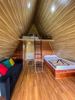 Un acogedor dormitorio en el ático con una cama alta, un sofá y una escalera.