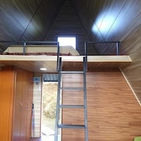 A room with a bunk bed, wooden walls, a ladder, and a window.