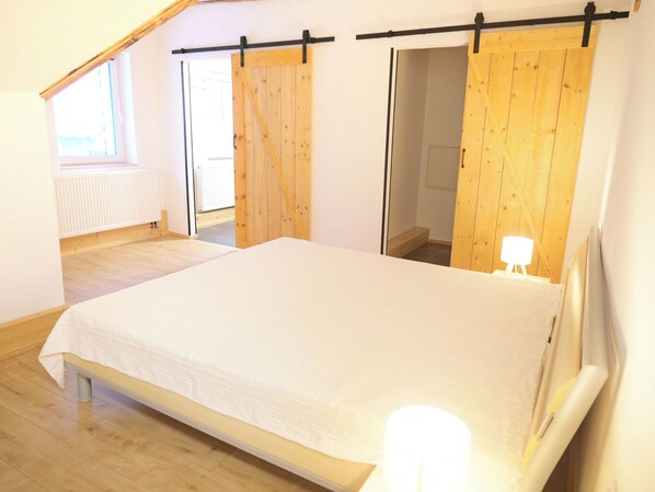 A bedroom with a bed, wooden floor, a window, and a door with a curtain.