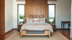 Een moderne slaapkamer met een groot bed, houten hoofdbord, nachtlampjes en uitzicht op groen door de ramen.