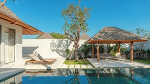 Een zwembad met een houten terras, ligbedden en een pergola.