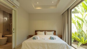 A modern hotel room with a large bed, a bathroom, and a view of tropical plants. - Famous 5 Trichada Resort  4-Bedroom V164 (Choeng Thale)