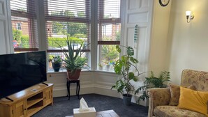 A living room with a TV, a coffee table with magazines, a sofa, and a potted plant by the window. - Victorian terrace house (Edinburgh)