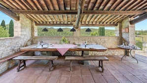 Un espace extérieur aménagé pour les repas, avec des murs en pierre, des poutres en bois et une vue sur la campagne.
