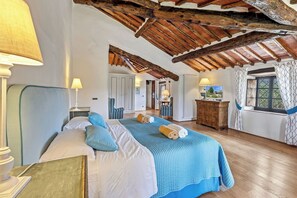 A bedroom with a wooden ceiling, a bed with blue bedding, a dresser, and a window with curtains. - Dimora del Chianti, stunning Tuscan stone villa surrounded by vineyards in the heart of Chianti (Rietine)