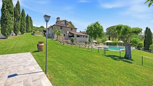 Une maison en pierre avec une piscine, entourée d’une pelouse bien entretenue et d’arbres.