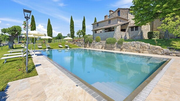 Une piscine avec des chaises longues, une maison en pierre et un ciel dégagé.
