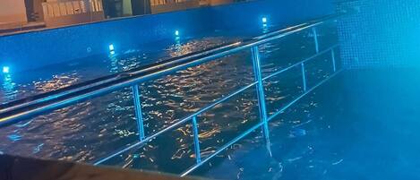 A nighttime view of a hotel with a swimming pool, illuminated by blue lights.