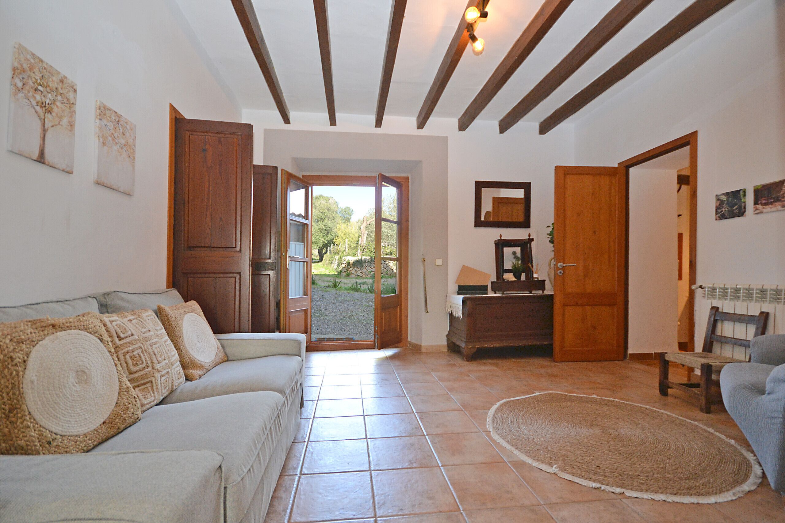 A living room with a sofa, a rug, wooden beams on the ceiling, and a door leading outside.