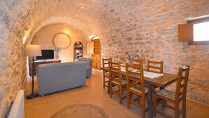 A stone-walled dining area with a wooden table and chairs, a sofa, and a television in a corner. - Rafal baix - idyllic country house with private pool (Son Servera)