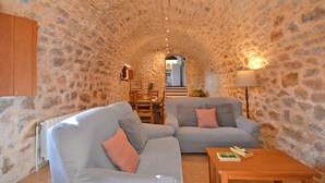 A cozy living room with stone walls, a wooden cabinet, a sofa, a table, and a lamp. - Rafal baix - idyllic country house with private pool (Son Servera)