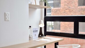 Um espaço de trabalho moderno com uma escrivaninha de madeira, uma luminária branca, uma garrafa, uma placa e uma cesta branca.