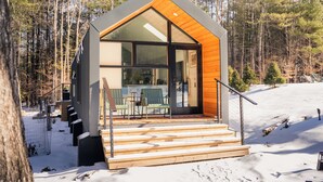 A modern cabin with a wooden exterior, large glass windows, and a wooden staircase leading to the entrance.