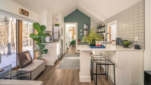 A modern kitchen with white cabinets, a green accent wall, and a large window overlooking a snowy landscape.